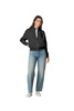 A woman wearing a black full-zip jacket and blue jeans, standing with one hand on her hip. The jacket has a logo.