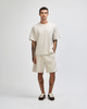 A model wears a light beige heavyweight cotton unisex boxy t-shirt and matching shorts, featuring a logo.
