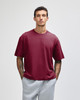 A maroon unisex boxy t-shirt displayed on a model, paired with grey sweatpants. The shirt features a logo.