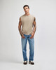 A light beige unisex sleeveless muscle t-shirt worn with blue jeans, featuring a logo on the shirt.