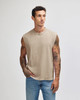 A sleeveless, heavyweight cotton muscle t-shirt in beige, worn by a model with tattoos, paired with blue jeans.