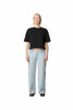 A black mid-length boxy top paired with light blue trousers, worn by a model standing upright. The outfit features a casual style.