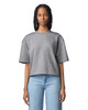 A woman stands wearing a grey mid-length boxy top, paired with light blue jeans. The top features a logo.