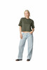 A woman stands wearing an olive green boxy top and light blue wide-leg jeans. The outfit is casual and stylish.