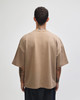 A unisex oversized boxy top in a light brown colour, featuring a minimal design and a branding logo.