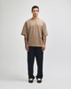 A model wearing a brown oversized boxy top paired with dark pants, standing against a neutral background.