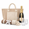 A striped tote bag, a bottle of champagne, two glasses, and a rolled blanket with a ribbon.