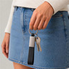 A woman is holding a black and silver keytag with keys attached, wearing a denim skirt and a light sweater.