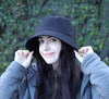 A black bucket hat featured on a model with long dark hair, set against a green backdrop. The hat has a logo on it.