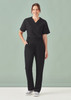 A woman wearing black unisex straight leg scrub pants and a matching top, standing against a plain backdrop.