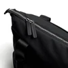 A black tote bag features a zip closure with leather zip pulls and a sturdy handle. It has a sleek, minimal design.