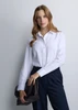 A white long sleeve women's shirt with a collar, paired with dark trousers. The model holds a dark clutch bag.