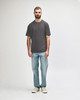 A midweight adult t-shirt in olive green, paired with black jeans and sneakers. The model is walking.