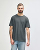 A man wearing a dark grey Gildan Softstyle adult T-shirt, paired with light blue jeans. The t-shirt has a logo.