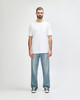 A man stands wearing a plain white Gildan Softstyle adult T-shirt paired with light blue jeans.