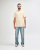 A model stands wearing a cream Gildan Softstyle adult T-shirt paired with light blue jeans and white sneakers.