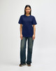 A navy Gildan Softstyle adult T-shirt displayed on a male model, paired with light blue jeans and white shoes.