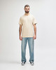 A light beige Gildan Softstyle adult T-shirt displayed on a model, paired with blue jeans. The model stands on a plain background.