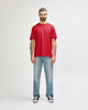 A red Gildan Softstyle adult T-shirt displayed on a male model, paired with light blue jeans. The shirt features a logo.