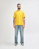 A man wearing a bright yellow Gildan Softstyle adult T-shirt and grey jeans, standing casually.