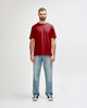 A model wearing a red Gildan Softstyle adult t-shirt paired with light blue jeans and white shoes. The shirt has a logo.