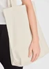 A cream canvas tote bag held by a person, featuring sturdy handles and a simple design.