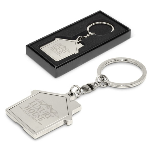A metal key ring shaped like a house, featuring a logo, presented in a black box. Silver in colour.