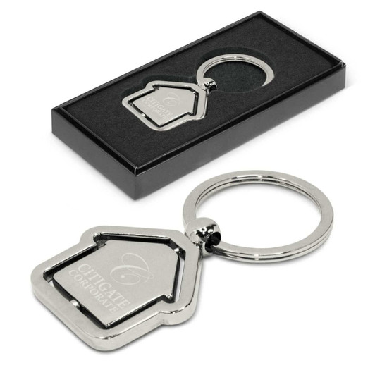 A metal key ring shaped like a house, featuring an engraved logo, presented in a sleek black gift box.