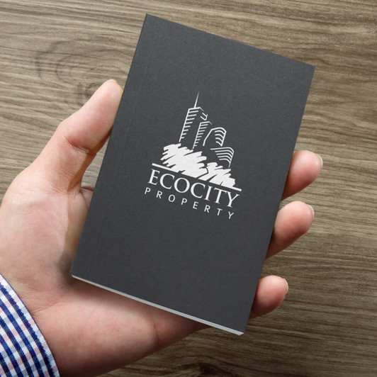 A small black notebook held in a hand, featuring a logo on the front.