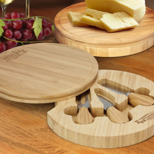 A round bamboo cheese board set featuring cheese, knives, and a decorative grape display.