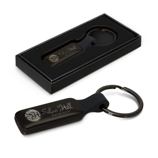A rectangular black key ring with a metal ring, presented in a black box, featuring a logo.