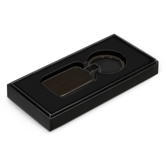 A black Astina key ring displayed in a black gift box with a soft interior.
