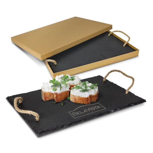A slate serving board in black with rope handles, presented with small cheese portions and a golden box.