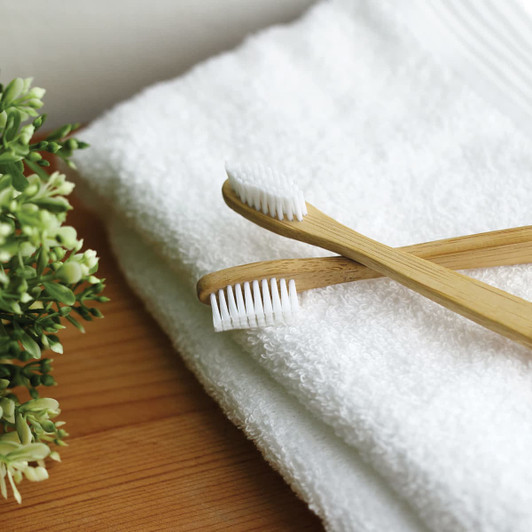 Two bamboo toothbrushes with white bristles resting on a white towel next to a small green plant.