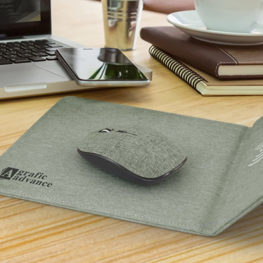 A grey wireless charging mouse mat with a mouse on a wooden desk, alongside a laptop and stationery.