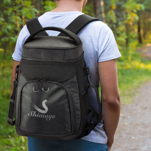 A black cooler backpack with a logo, carried on a person's back, set in a natural outdoor environment.
