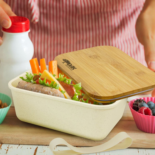 A lunch box with a bamboo lid contains a sandwich, salad, and carrot sticks, alongside a drink bottle and fruits.