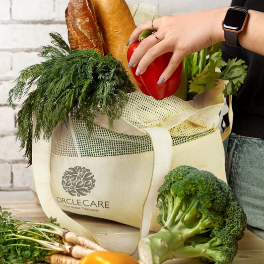 A cream-coloured cotton tote bag filled with fresh vegetables, including carrots, broccoli, and a red bell pepper.