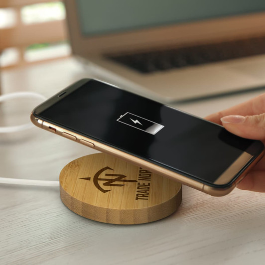 A bamboo wireless charger with a smartphone being placed on it, featuring a charging indicator on the phone's screen.