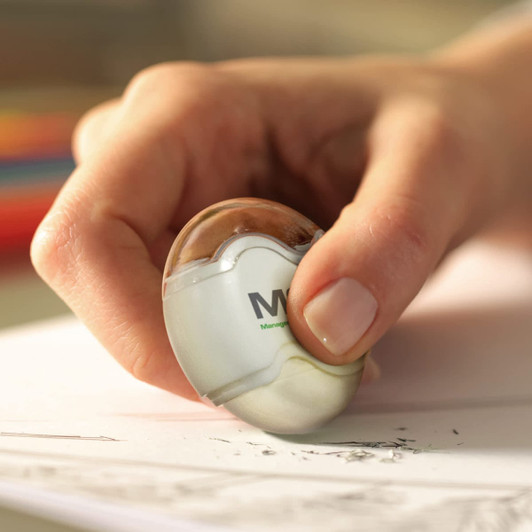 A pencil sharpener with an eraser, featuring a sleek design and held in a hand, with shavings on the paper below.