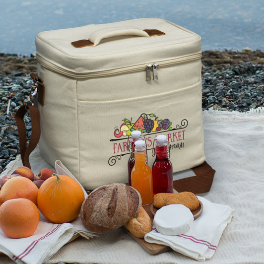A beige cooler bag with a logo, surrounded by fruits, glass bottles, and bread on a textured surface.