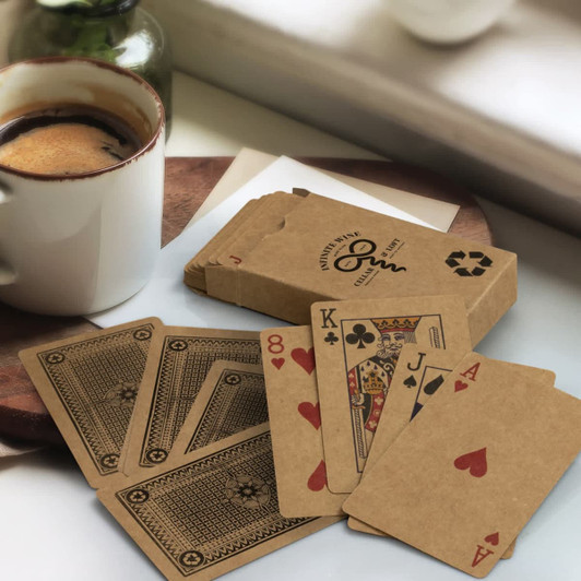 A set of brown Kraft playing cards displayed with an open card showing the Ace of Hearts, beside a coffee cup.