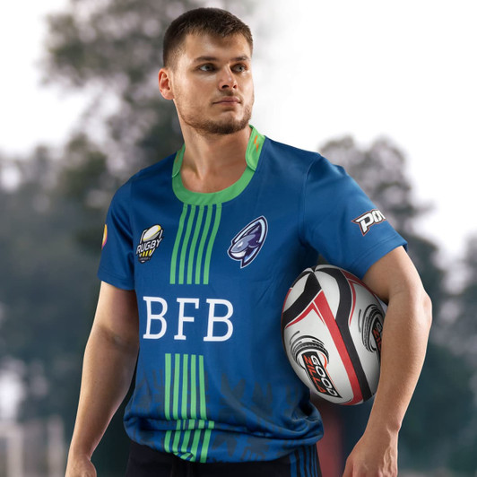 A man wearing a blue rugby T-shirt with green accents, holding a rugby ball. The shirt features a logo.