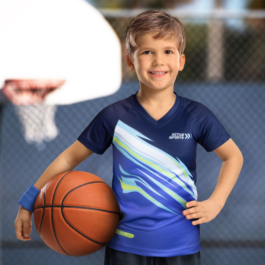 A boy in a blue and green performance T-shirt holds a basketball, standing in front of a basketball hoop.