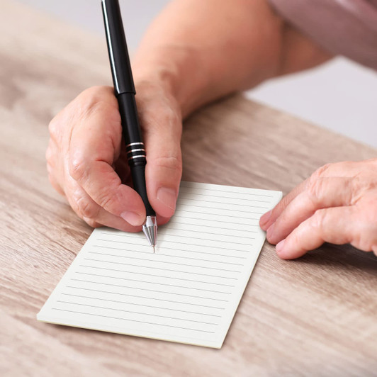 A notepad with lined pages in a light colour, held by a hand with a pen above it.