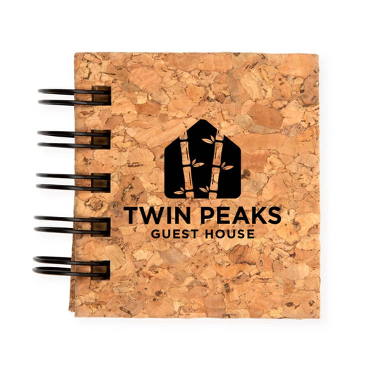 A cork notebook featuring a black spiral binding and the logo for "Twin Peaks Guest House" embossed on the cover.