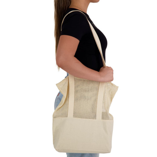A cream tote bag with mesh panels is being held by a person. The bag has shoulder straps and a spacious design.