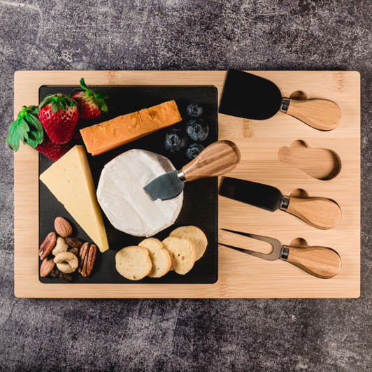 A bamboo slate cheese board featuring various cheeses, berries, nuts, and crackers, accompanied by serving utensils.