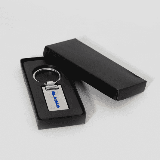 A silver keychain in a black presentation box, featuring a simple design and a logo.