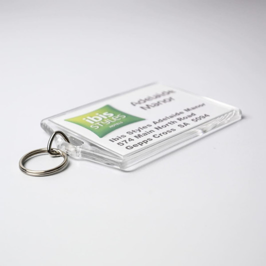 A clear hotel keychain with a keyring, featuring a logo. The background is predominantly white with green accents.